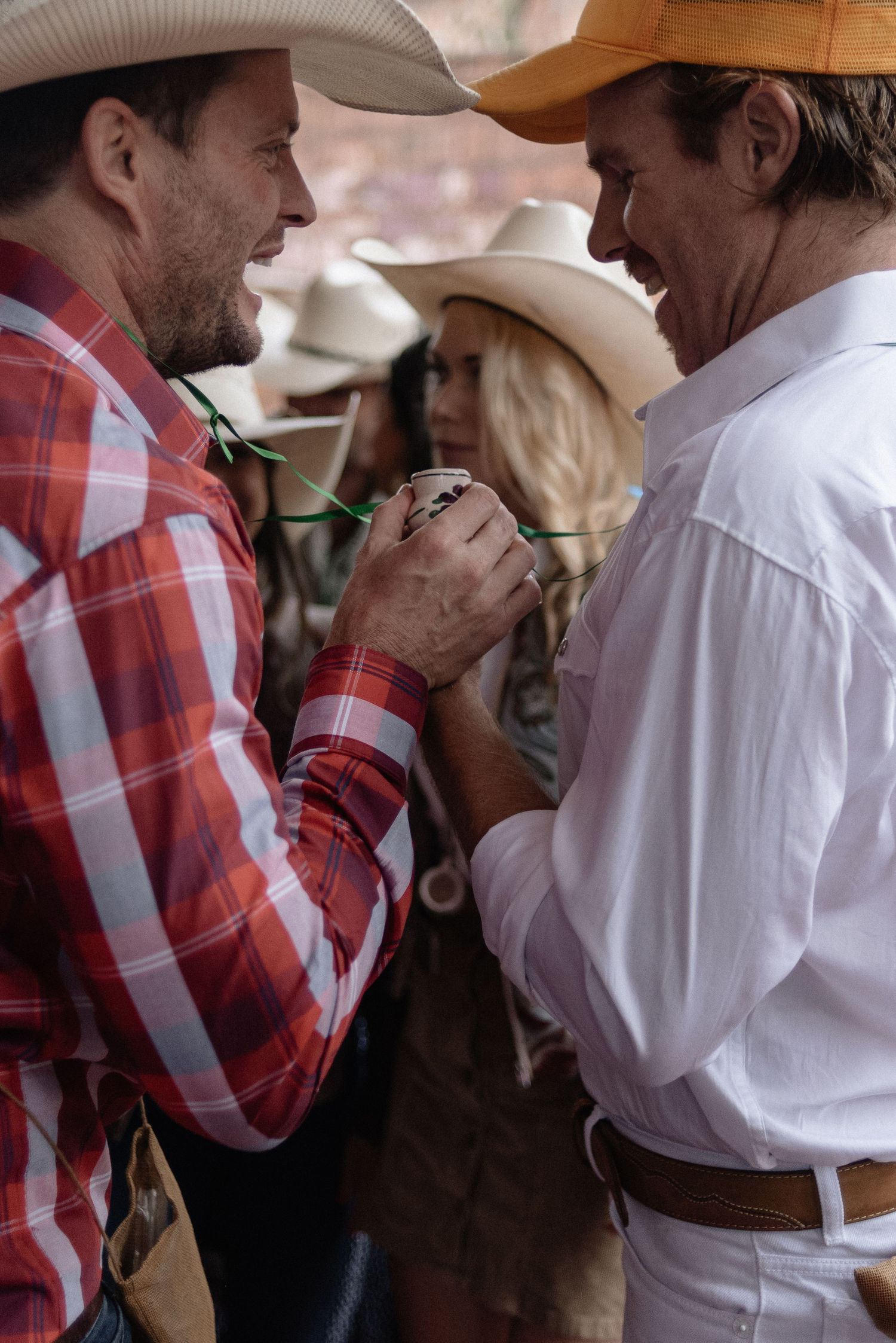 Two cowboys in cowboy hats having a close conversation at what appears to be a rodeo or western event.