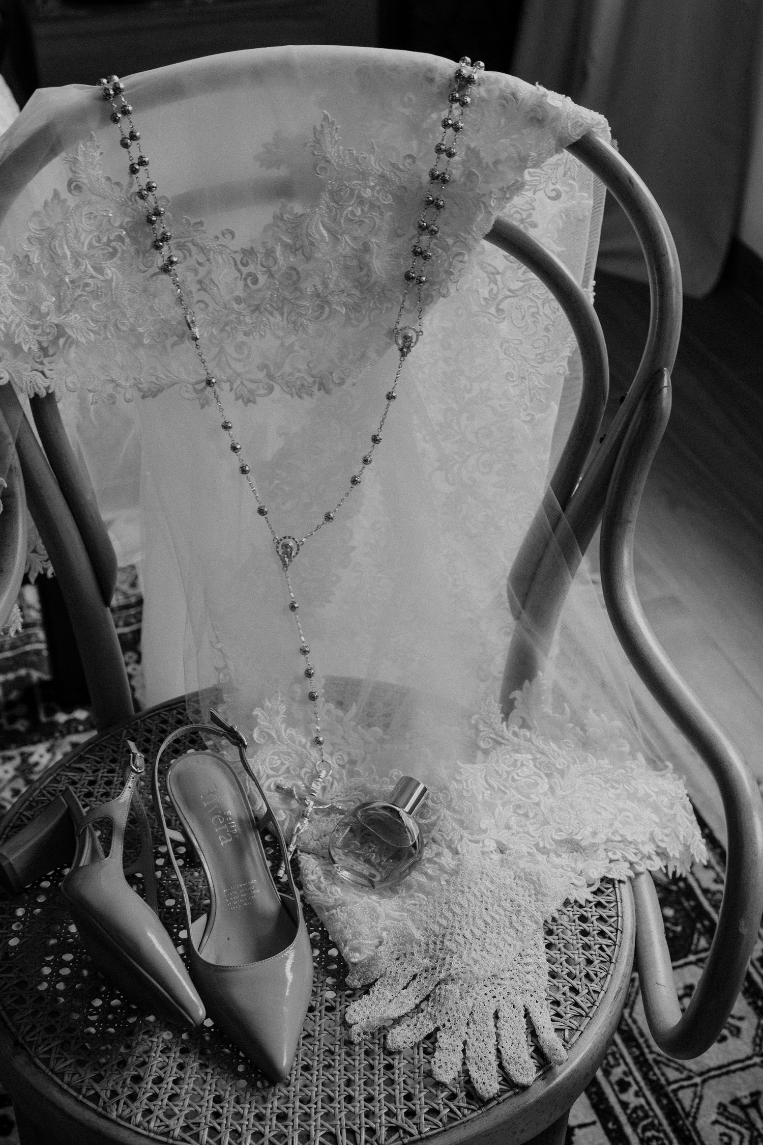 Wedding accessories including lace dress, delicate necklace, and heels arranged on an antique chair.