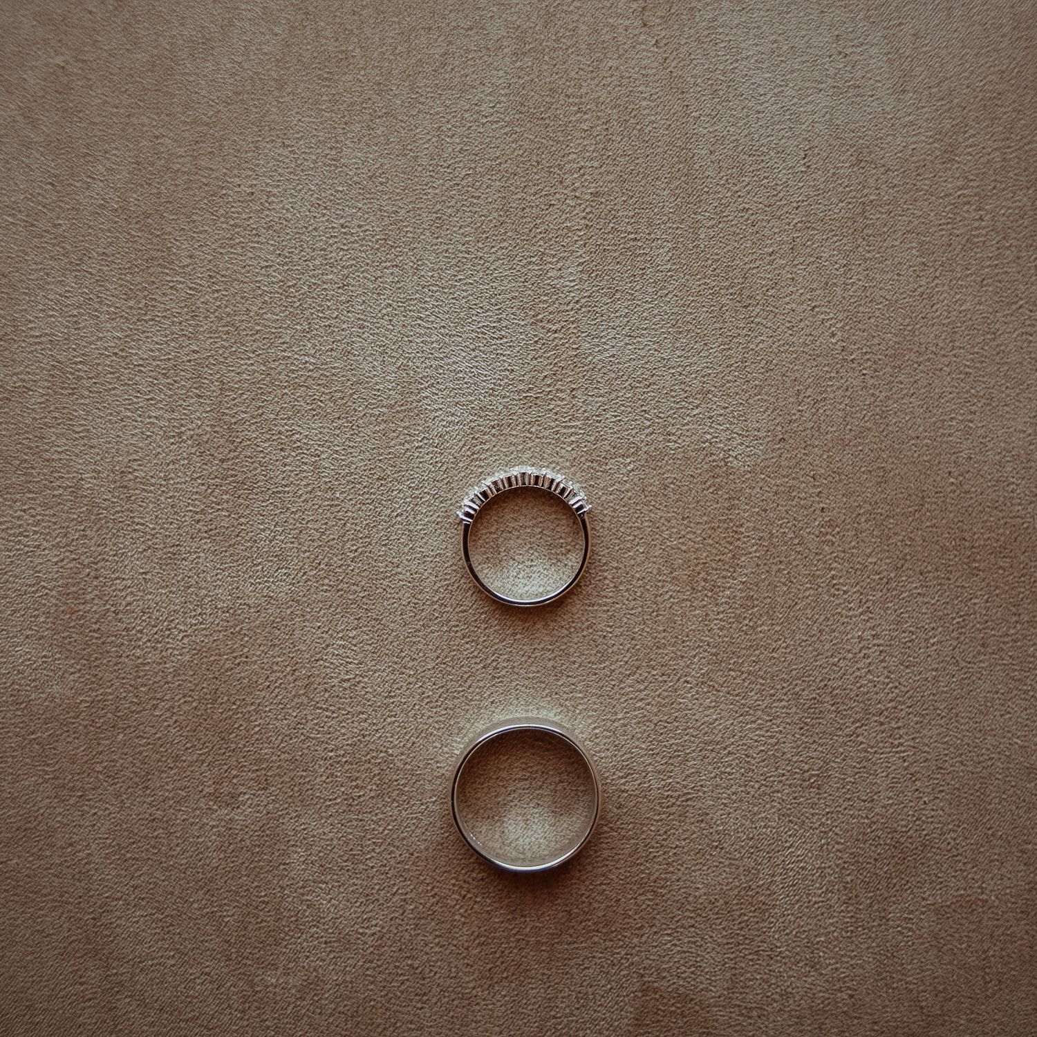Two elegant wedding rings photographed on a beige textured background.