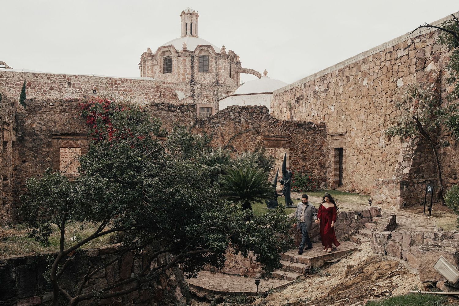 People walk through historic stone ruins with a church dome visible in the background.