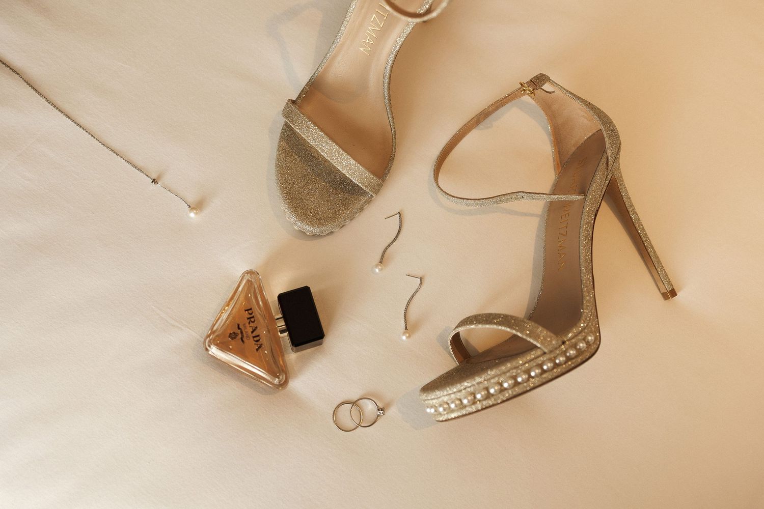 Elegant nude-colored strappy sandals and wedding rings arranged on a light beige background.