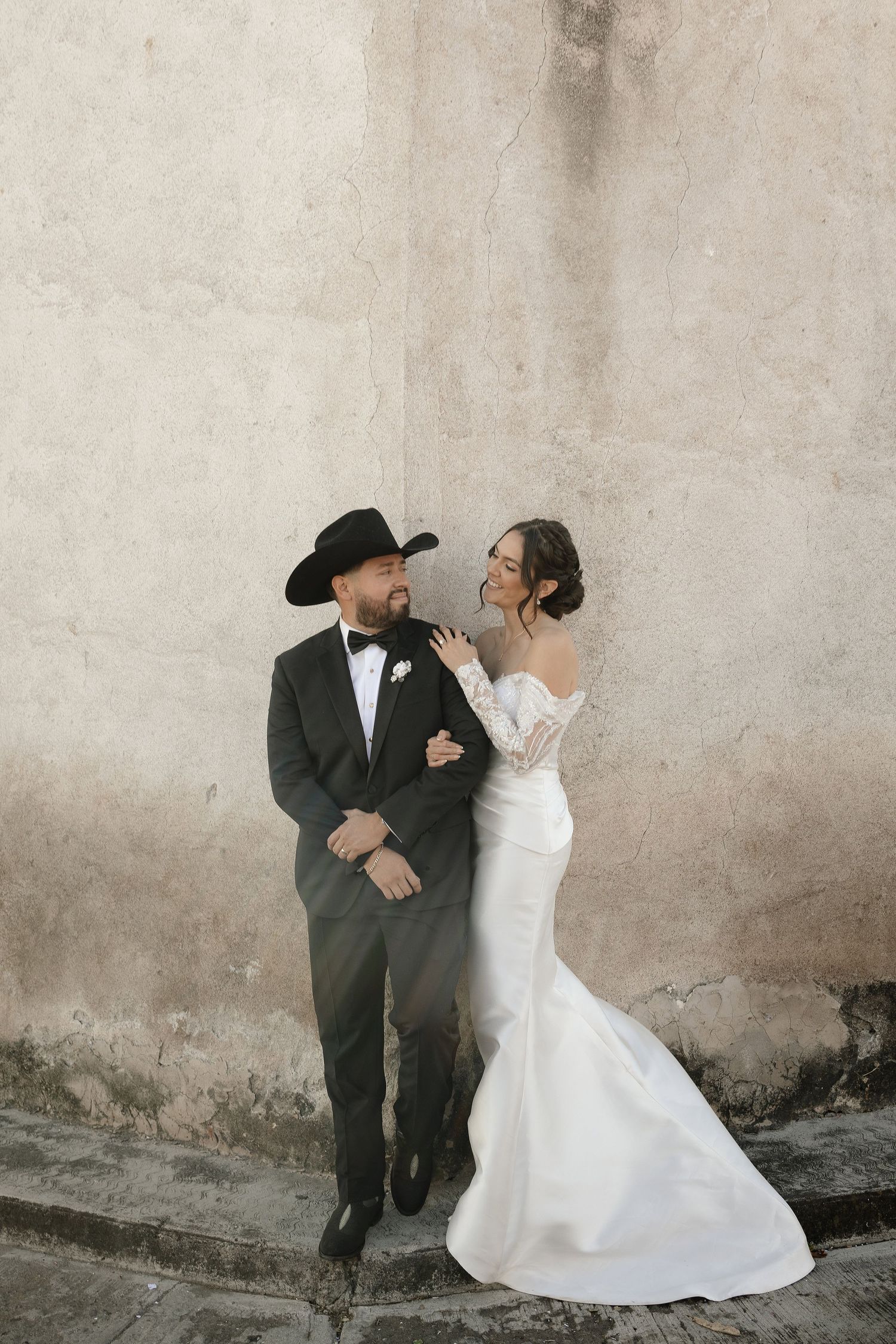 A couple in wedding attire shares a romantic moment against a textured wall in a four-panel photo sequence.