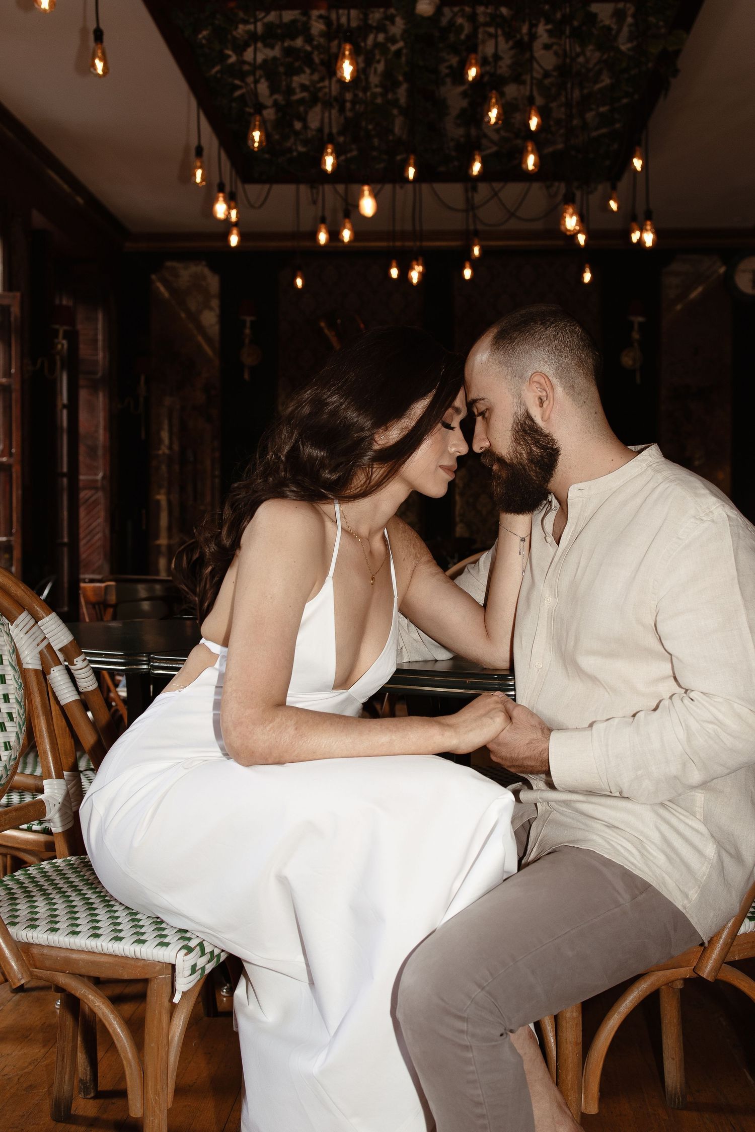 A couple shares an intimate moment in a dimly lit restaurant with hanging pendant lights above.