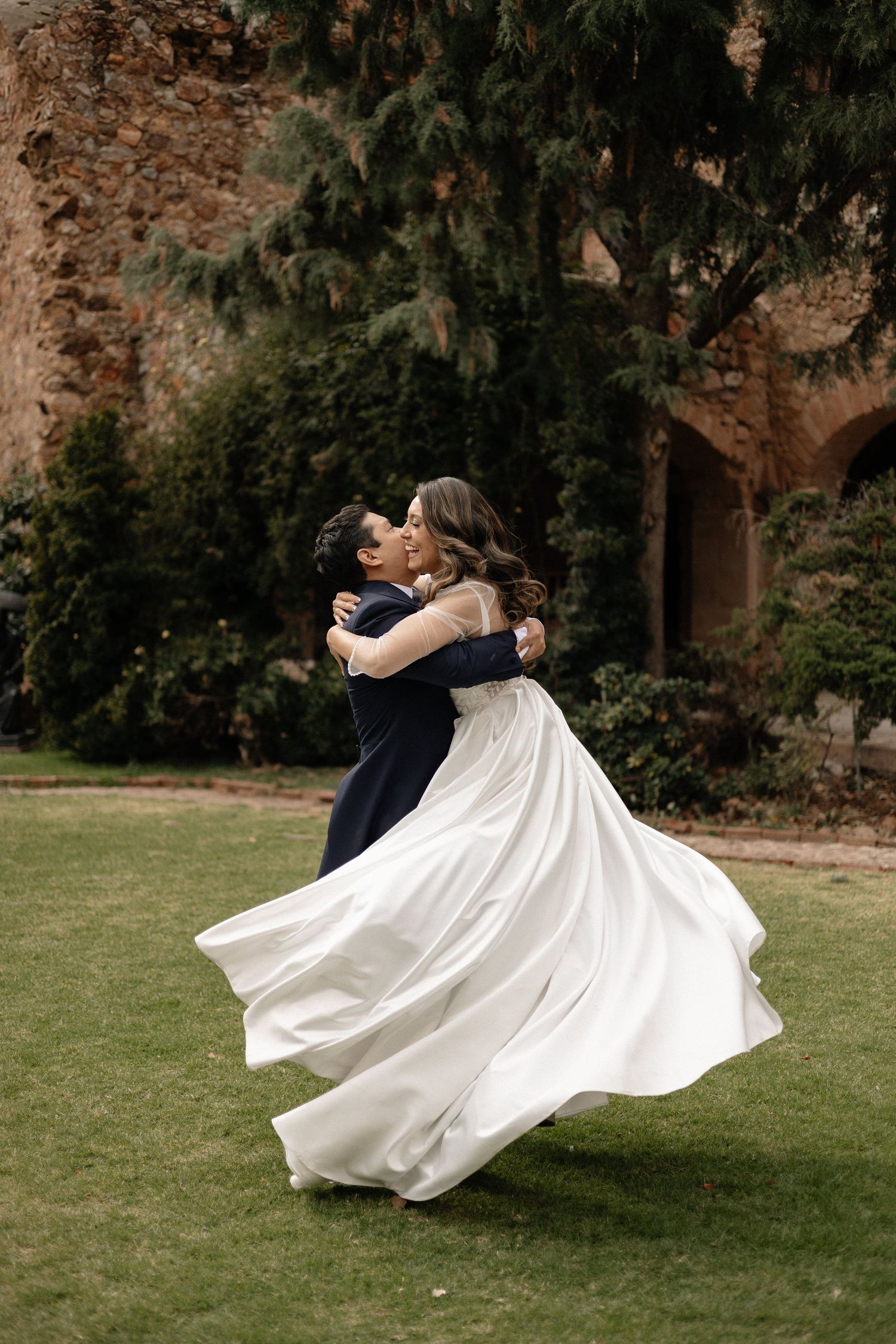 Couple dances on grass lawn as bride's white dress flows dramatically in elegant spinning motion.