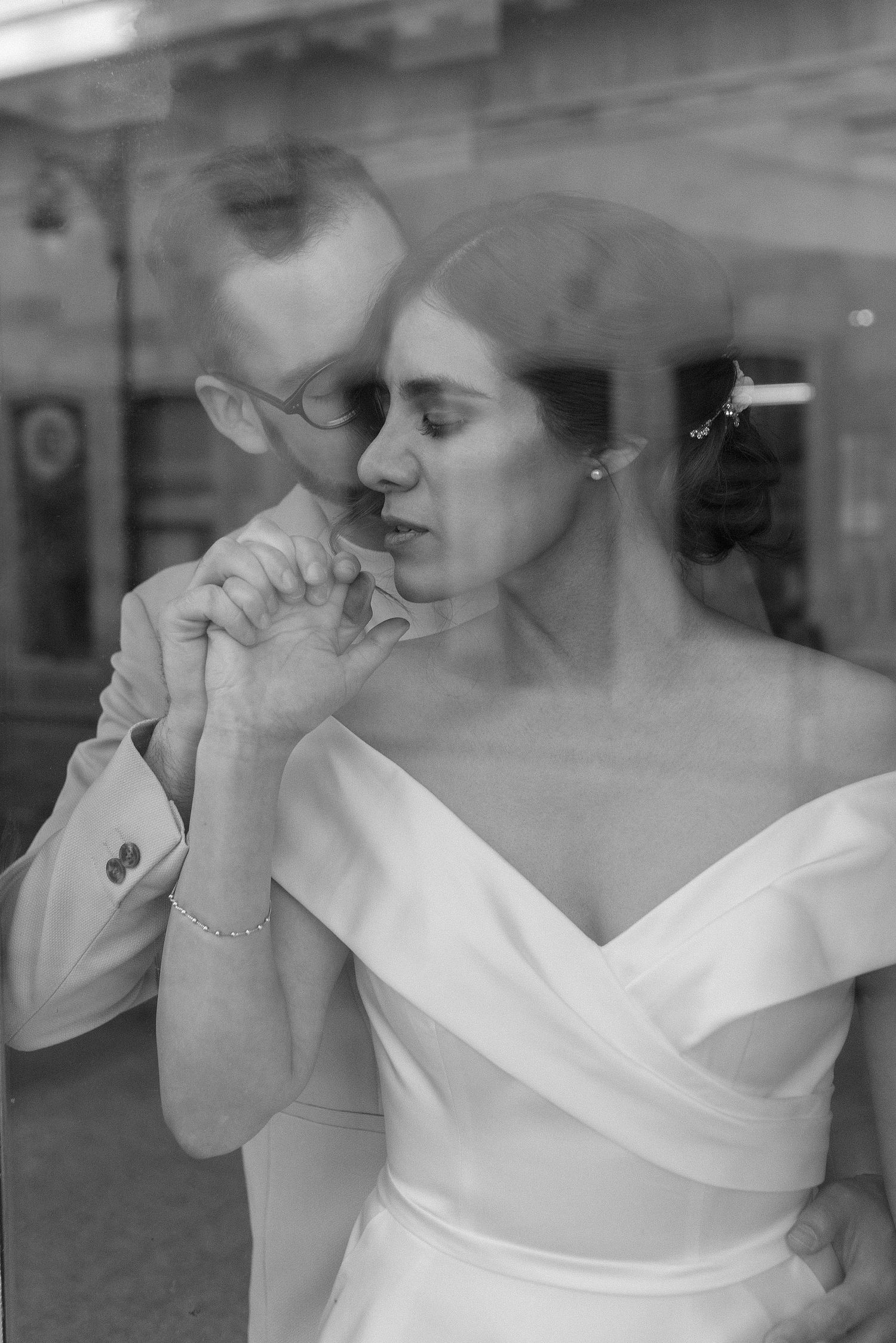 A bride in an elegant white dress holds a glass of champagne against a reflective window.