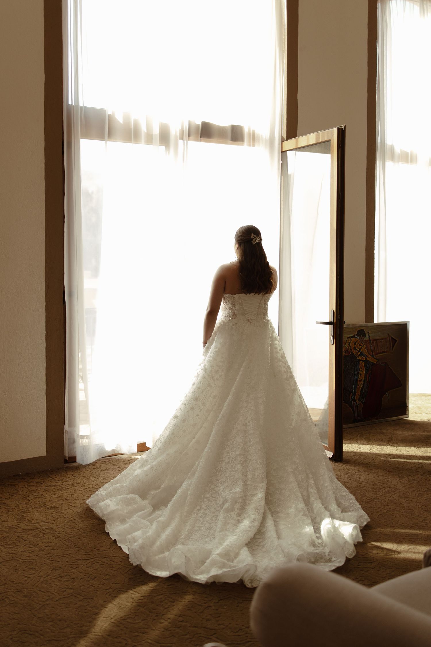 A flowing white wedding gown with a long train captured in silhouette against window light in multiple angles.