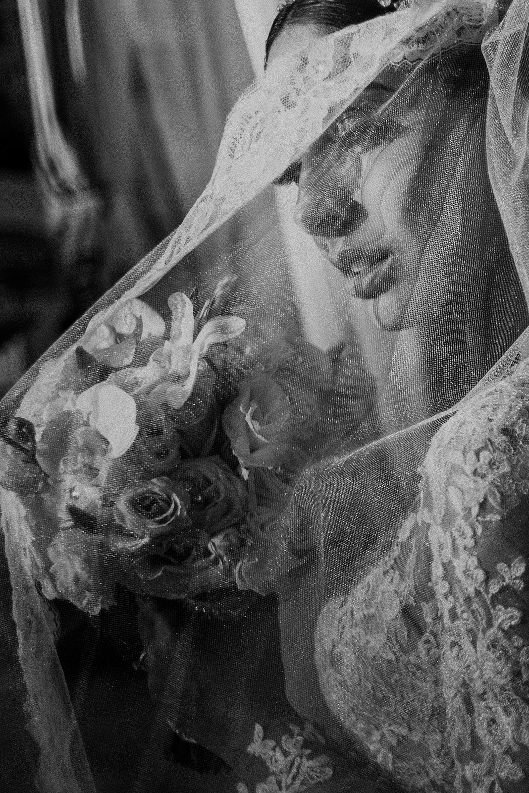Black and white close-up of bride with lace veil and floral bouquet.