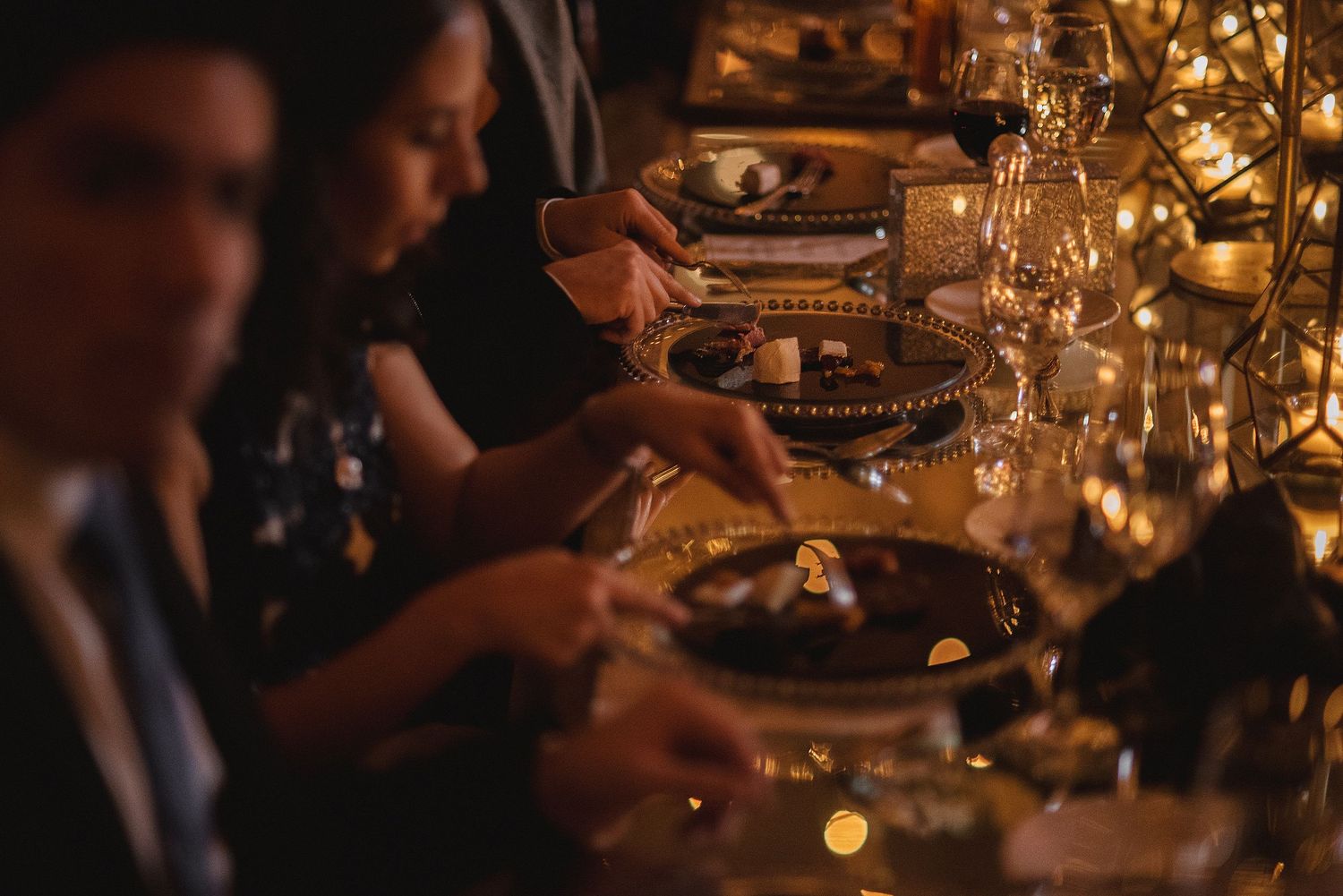 Atmospheric candlelit wedding reception dinner with elegant table settings and golden ambient lighting.