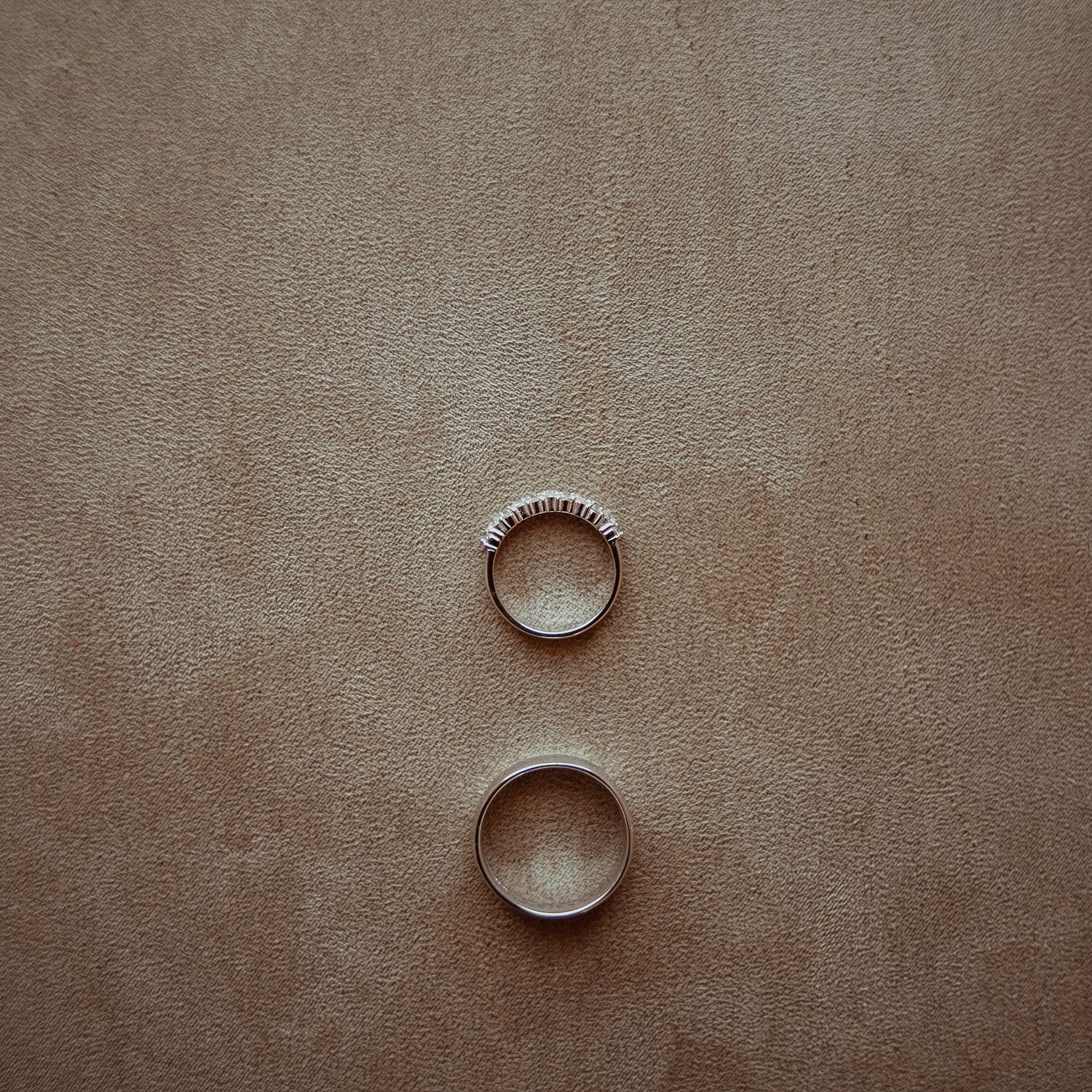 Wedding rings arranged on neutral beige fabric background.