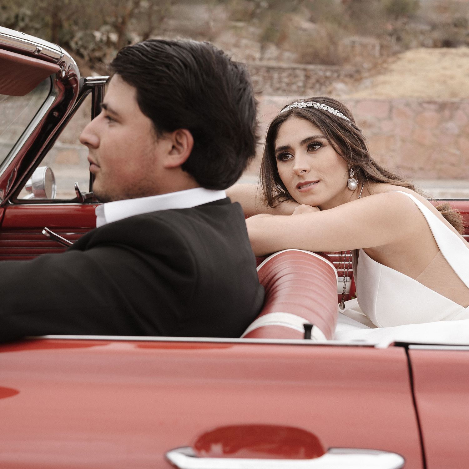 Newlyweds pose in vintage red convertible car.