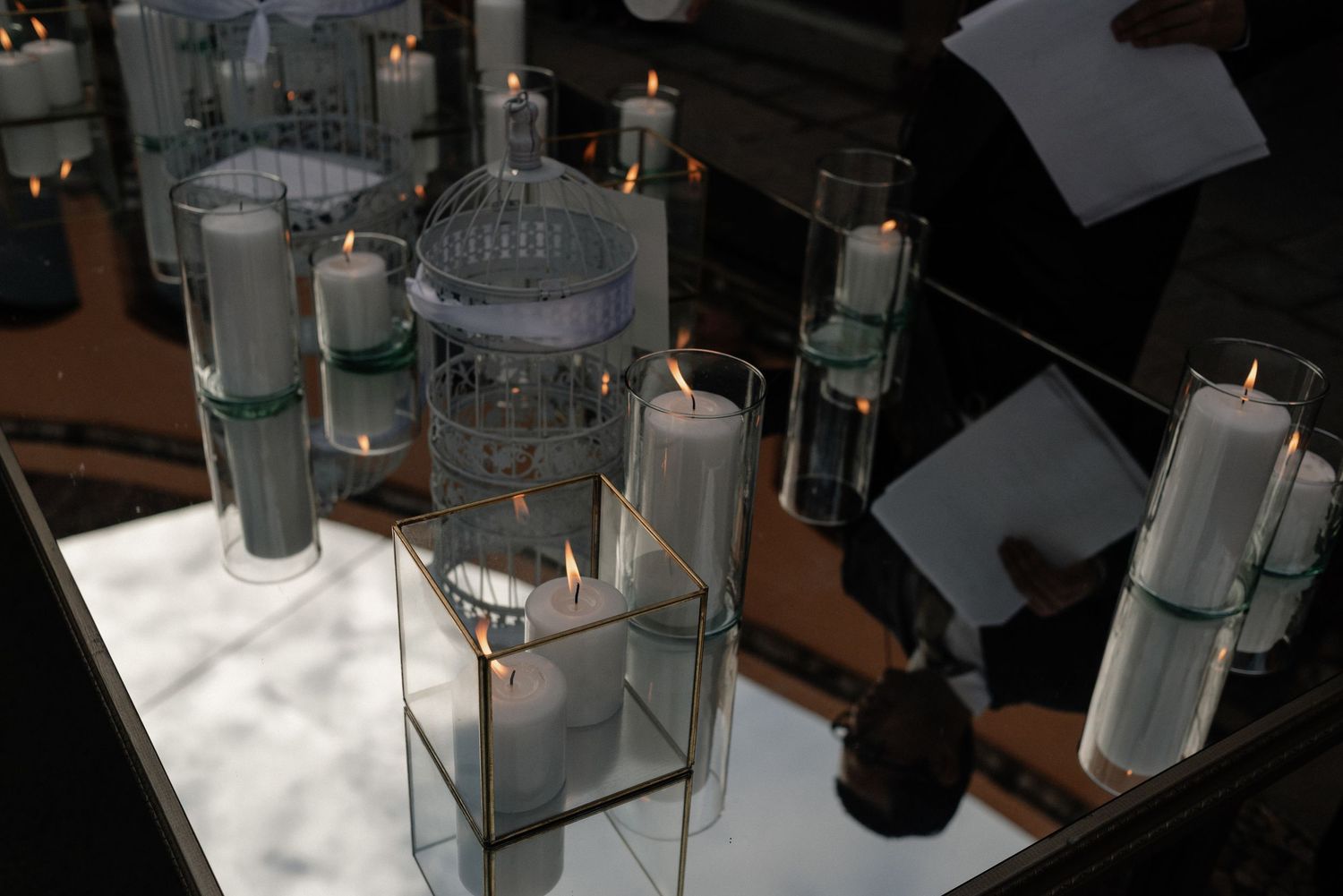 Glass candle holders and decorative jars displayed on a mirrored surface create an elegant table setting.