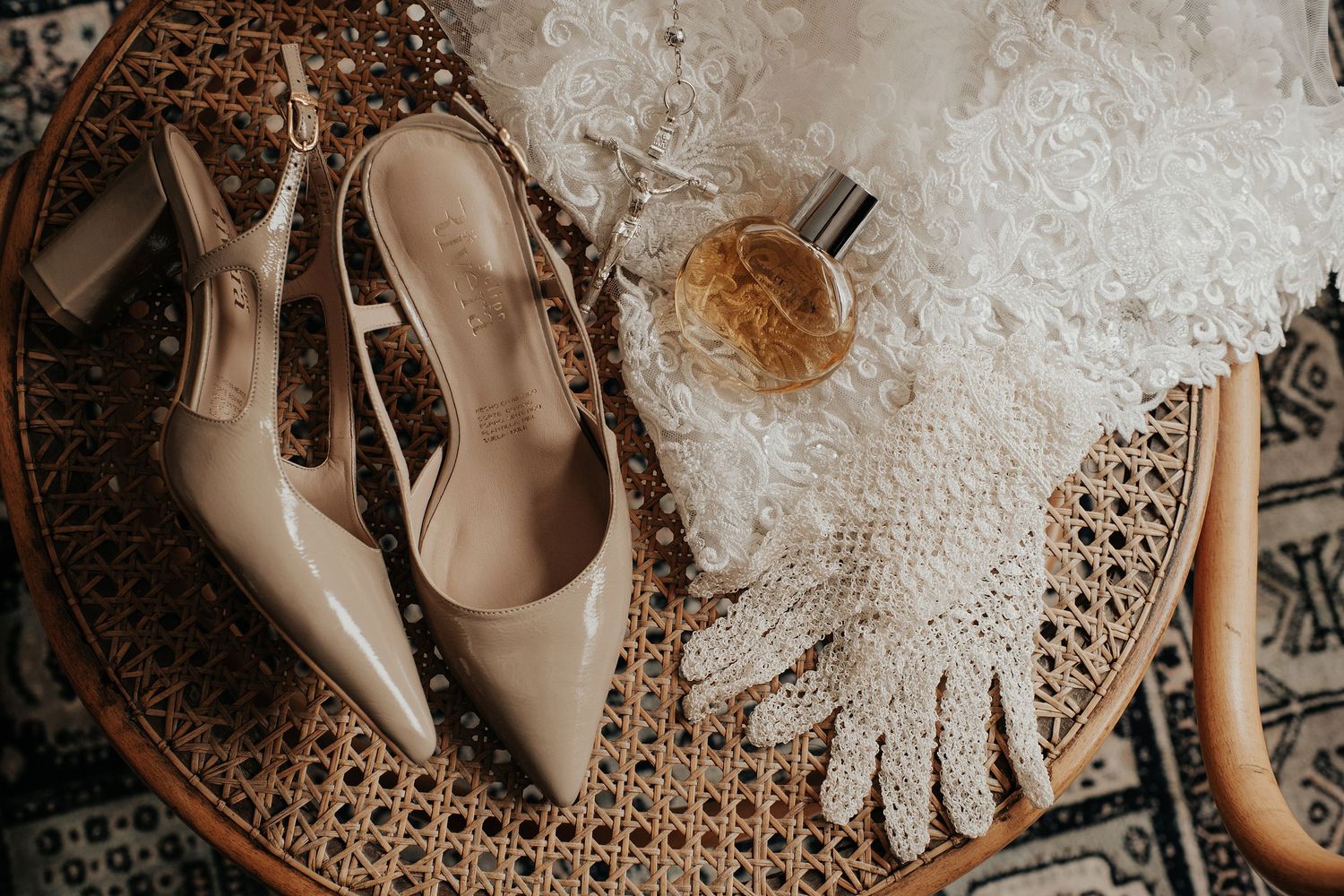 Wedding accessories including nude heels, lace gloves and perfume arranged on a wicker surface.