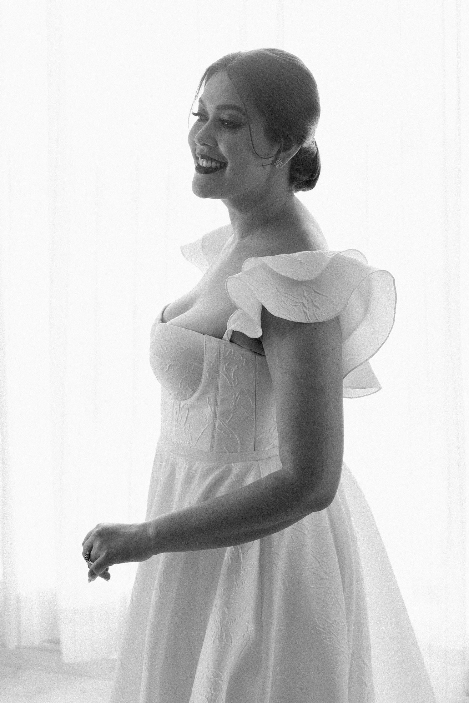 Black and white portrait of a bride in ruffled wedding dress laughing joyfully.