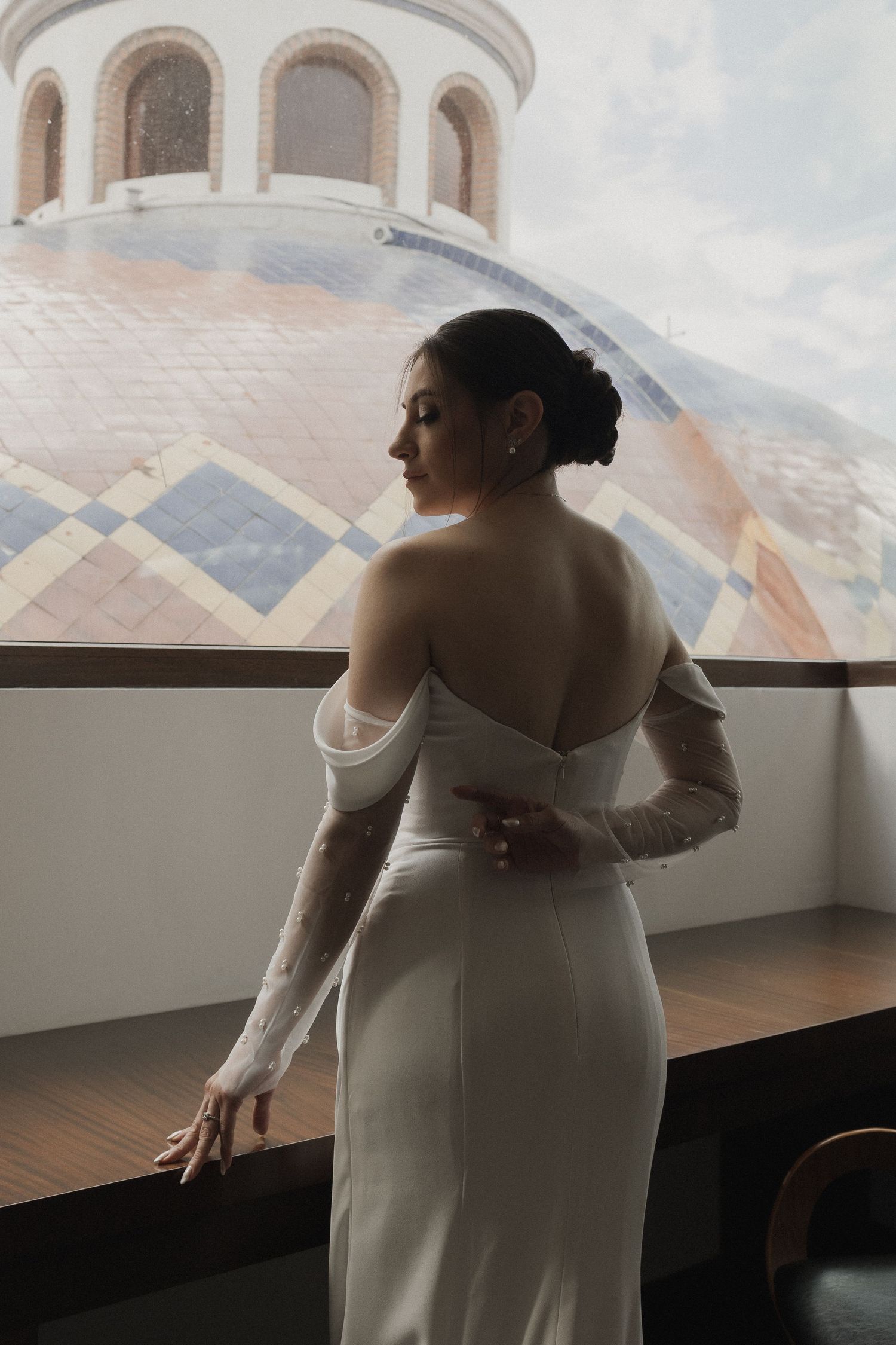 A bride in a simple white wedding dress stands by a window in a series of artistic silhouette shots.