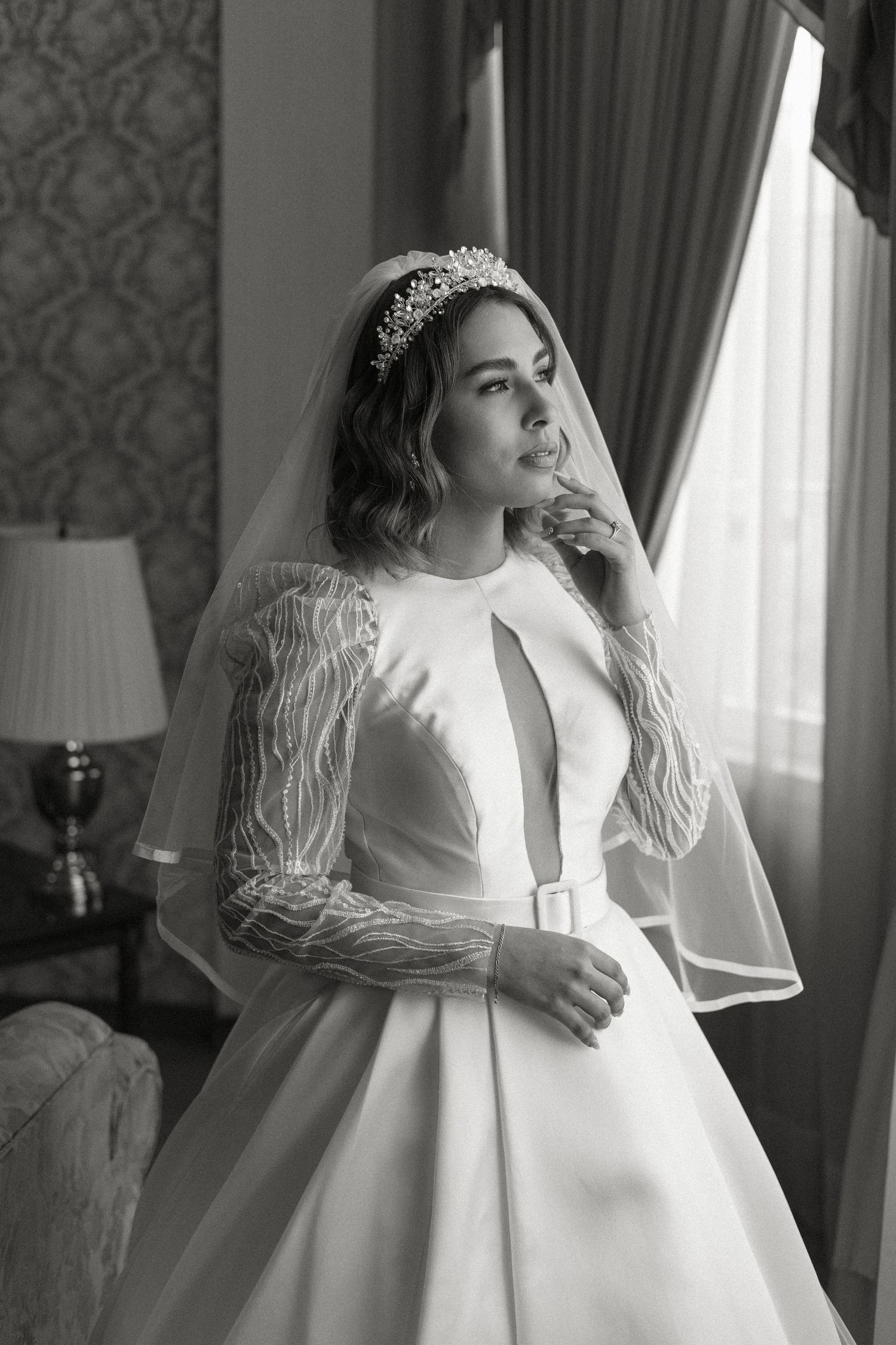 A bride in an elegant white long-sleeved wedding gown poses near a window in a series of black and white photographs.