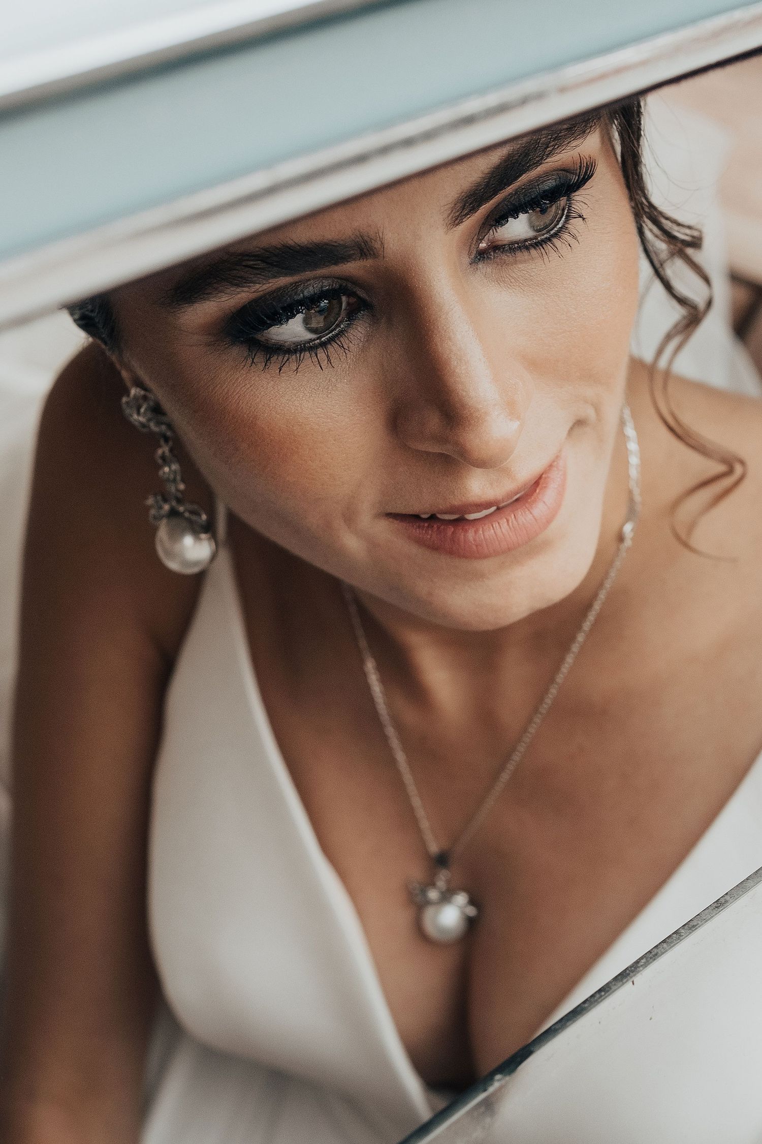 Close-up portrait of a bride wearing elegant pearl jewelry and dramatic eye makeup.
