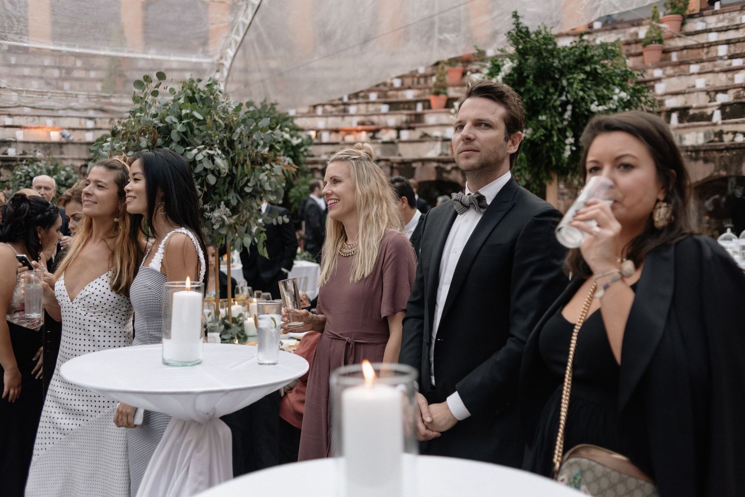 Wedding guests enjoying outdoor cocktail hour at a rustic brick venue with greenery and modern decor.