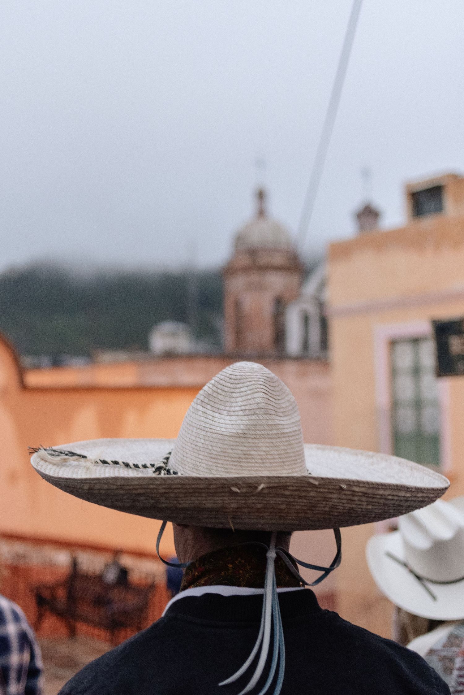 Back view of someone wearing a traditional Mexican sombrero hat against blurred colonial architecture in Mexico.