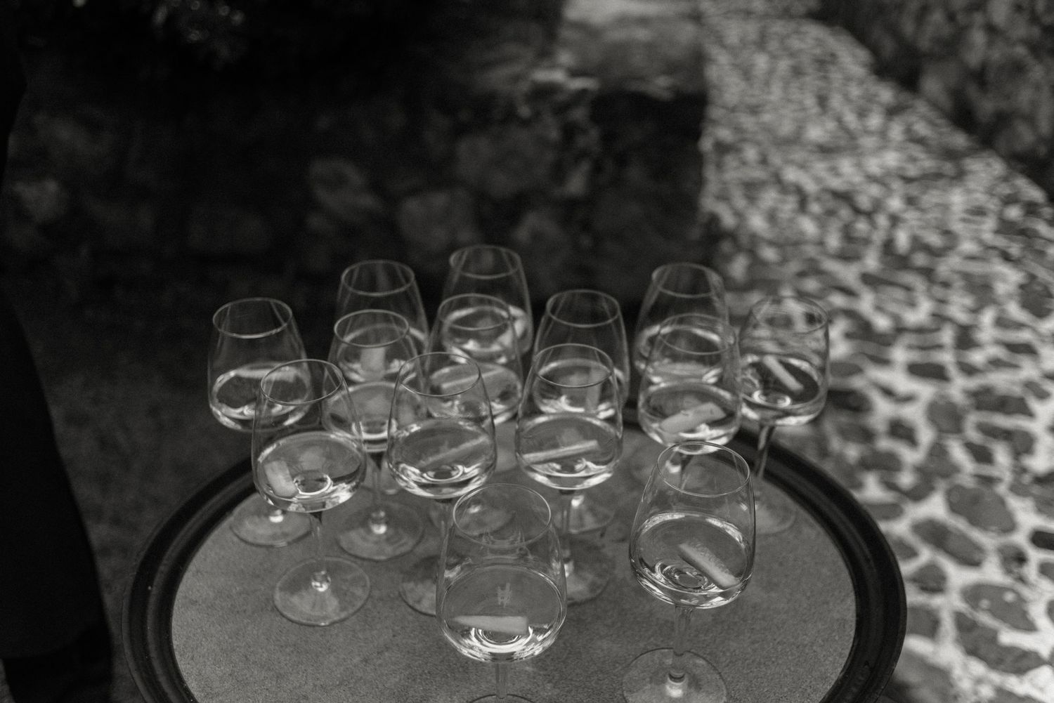 Empty wine glasses arranged on a round dark table with a stone pathway visible in the background.