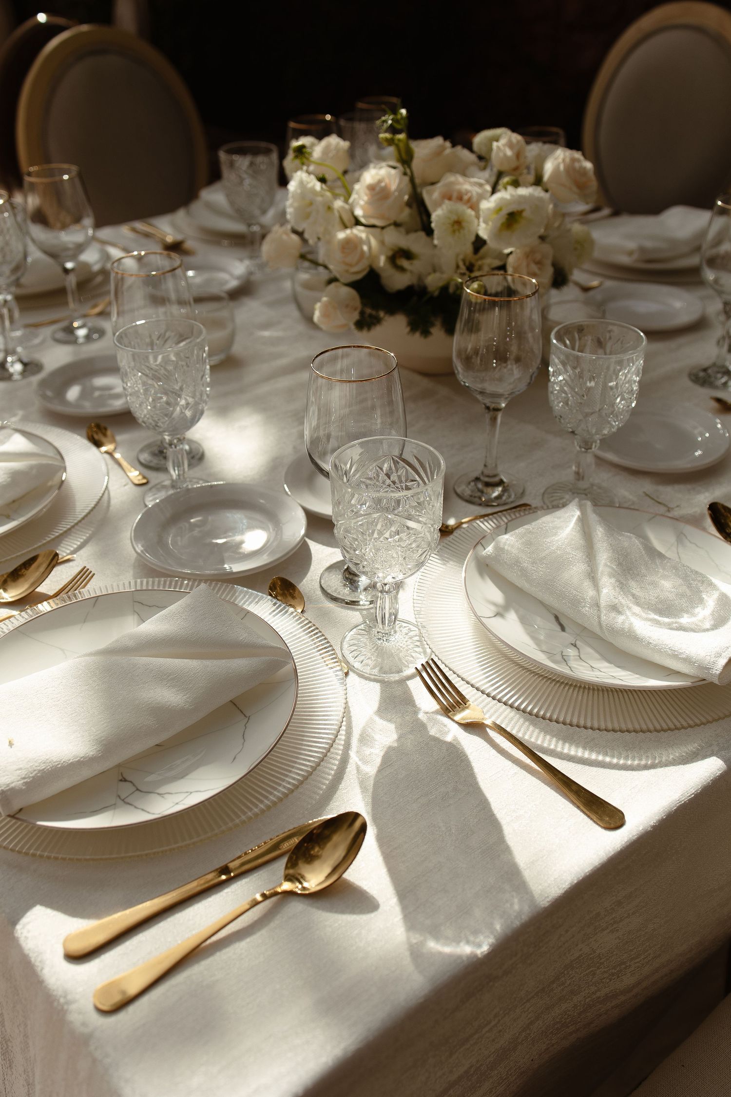 Elegant table setting with white flowers, crystal glasses and gold cutlery for wedding reception.