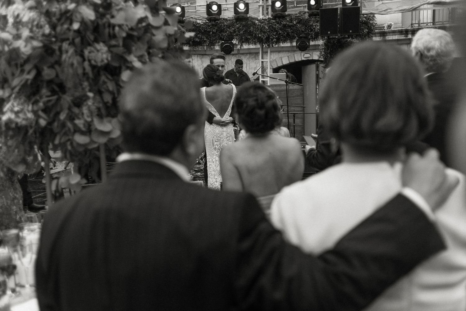 Black and white photo of an outdoor wedding ceremony with guests watching from behind as bride and groom stand at altar.