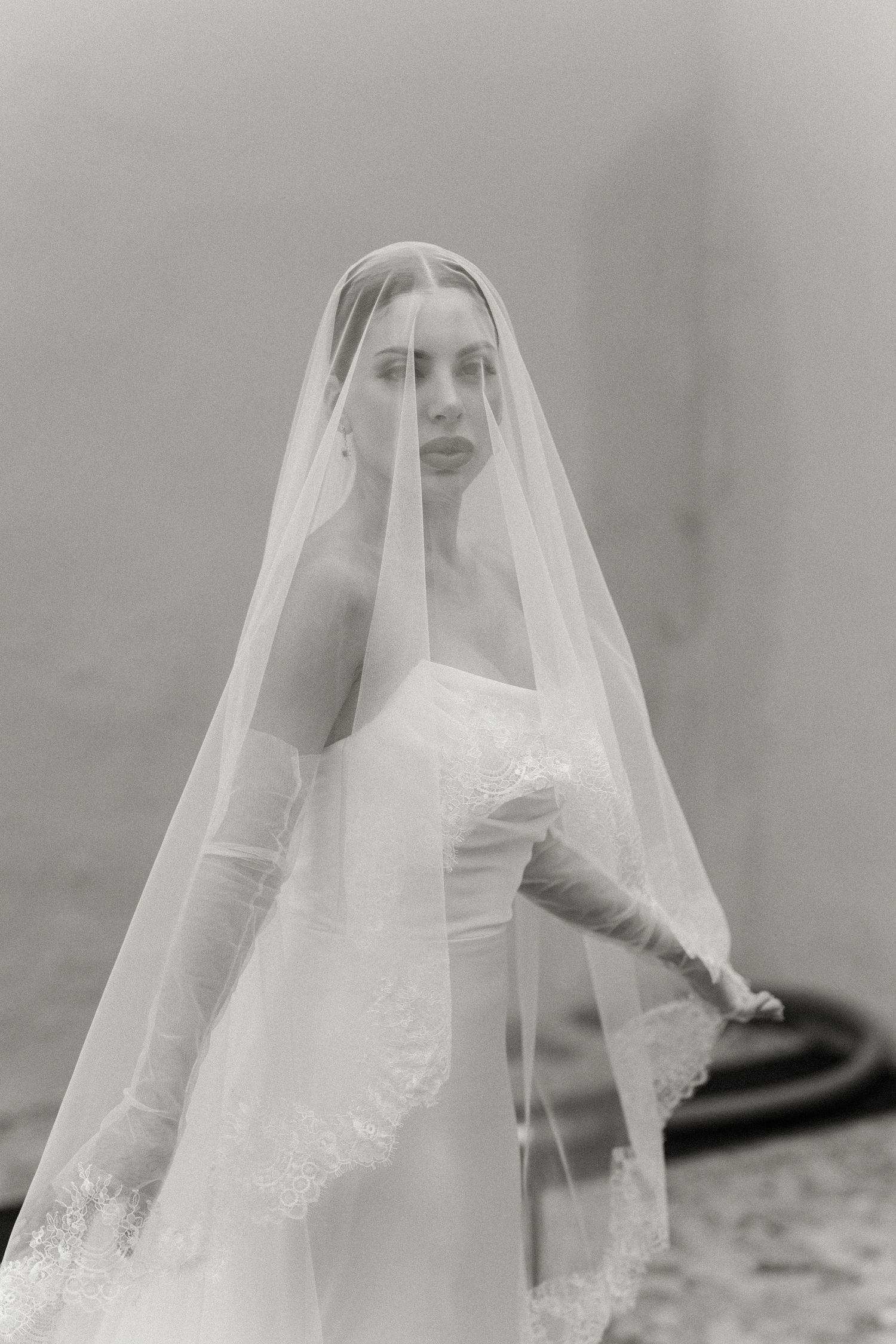 Black and white photo of a bride in a strapless gown, lace-trimmed veil, and white gloves posing elegantly.