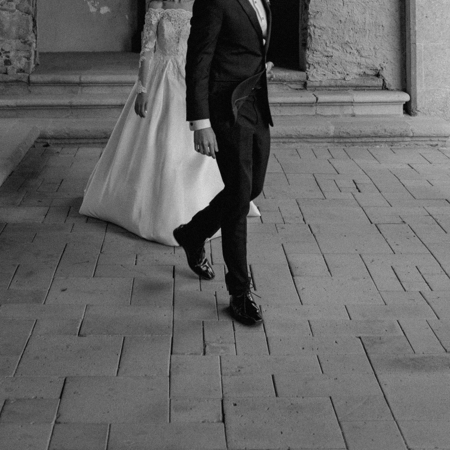 Black and white photo showing formal wedding attire details on stone pavement.