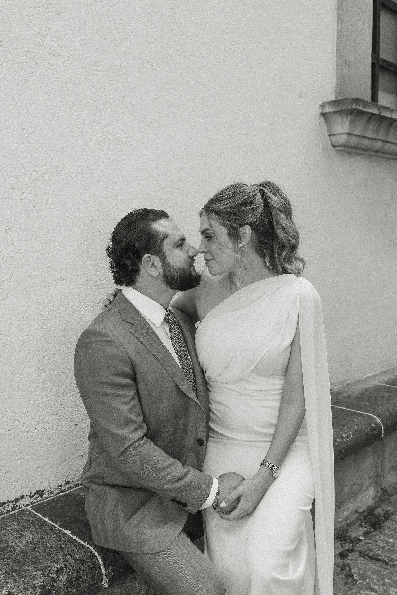 A romantic black and white wedding photo showing a tender moment between newlyweds in elegant attire.