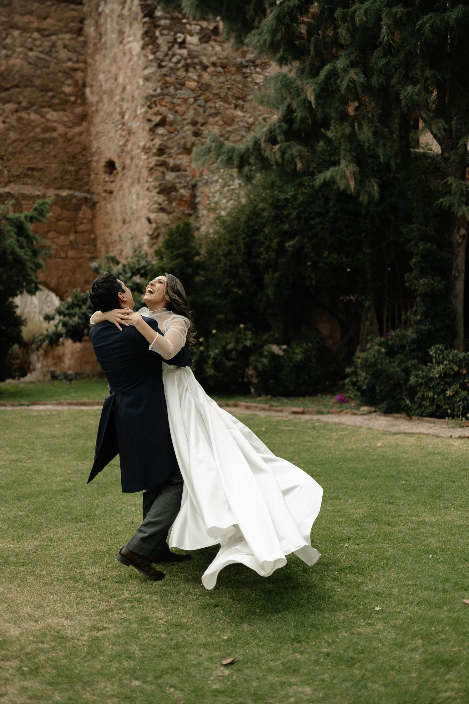 A romantic dip sequence shows a couple in wedding attire dancing on a grassy lawn against an old stone wall.