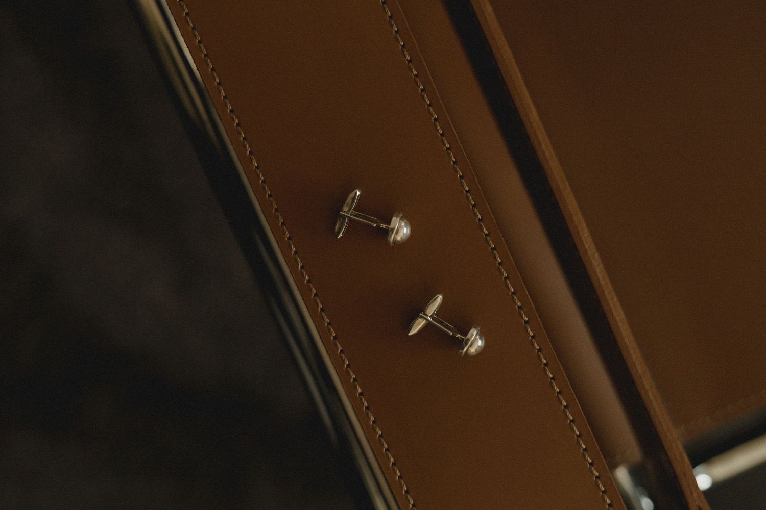 Macro close-up of a brown leather surface with metal rivets and stitching details showing quality craftsmanship.