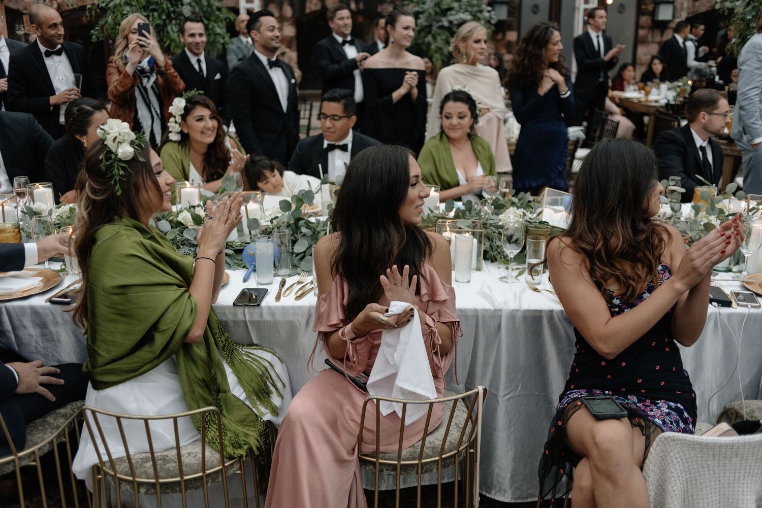 Wedding guests seated at elegant outdoor reception tables with green and pink dresses enjoying the celebration.