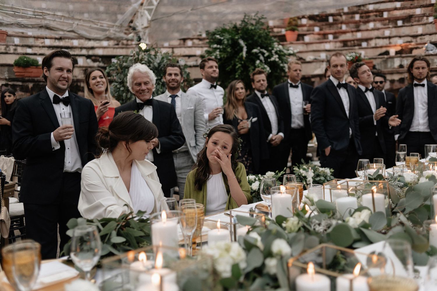Wedding reception guests laugh and share joyful moments at a beautifully decorated dinner table with candles and greenery.