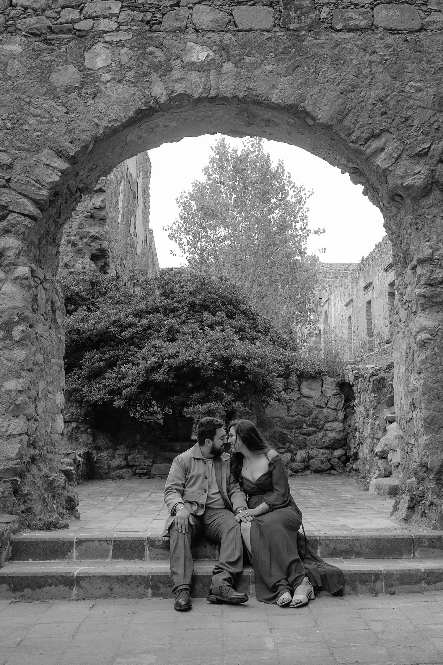 A romantic black and white moment under a stone archway at a historic site.