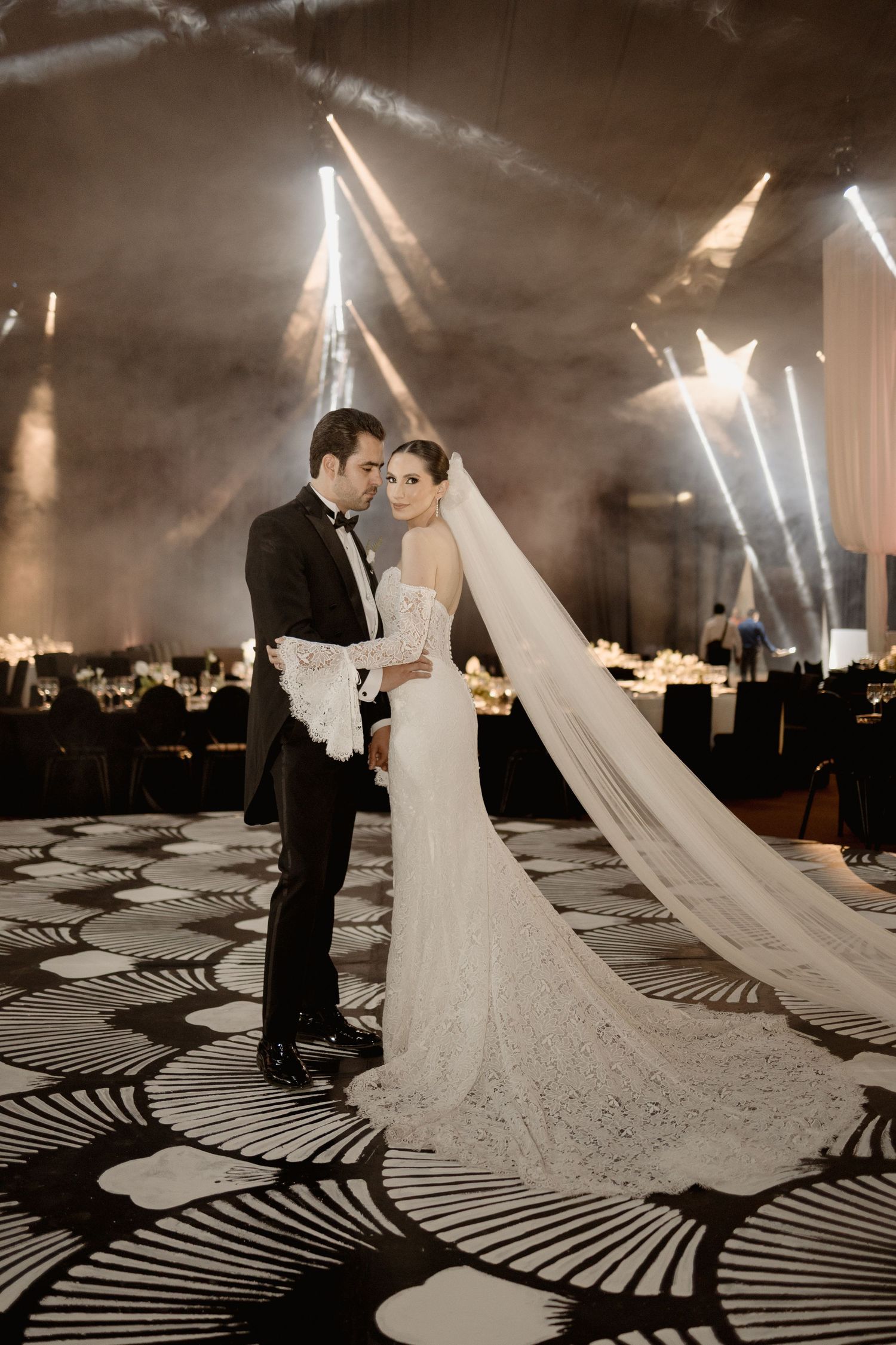 A couple shares an intimate moment on their wedding day with dramatic lighting and geometric shadows on the floor.