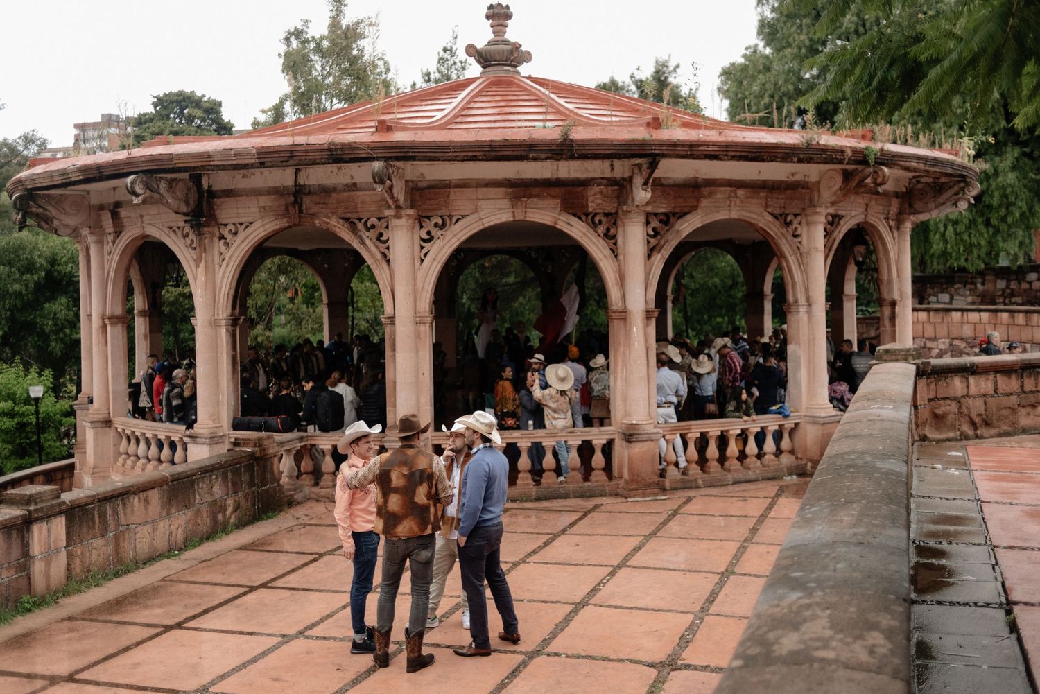 Visitors gather under an ornate Victorian-style gazebo with copper dome and stone railings in a historic garden setting.