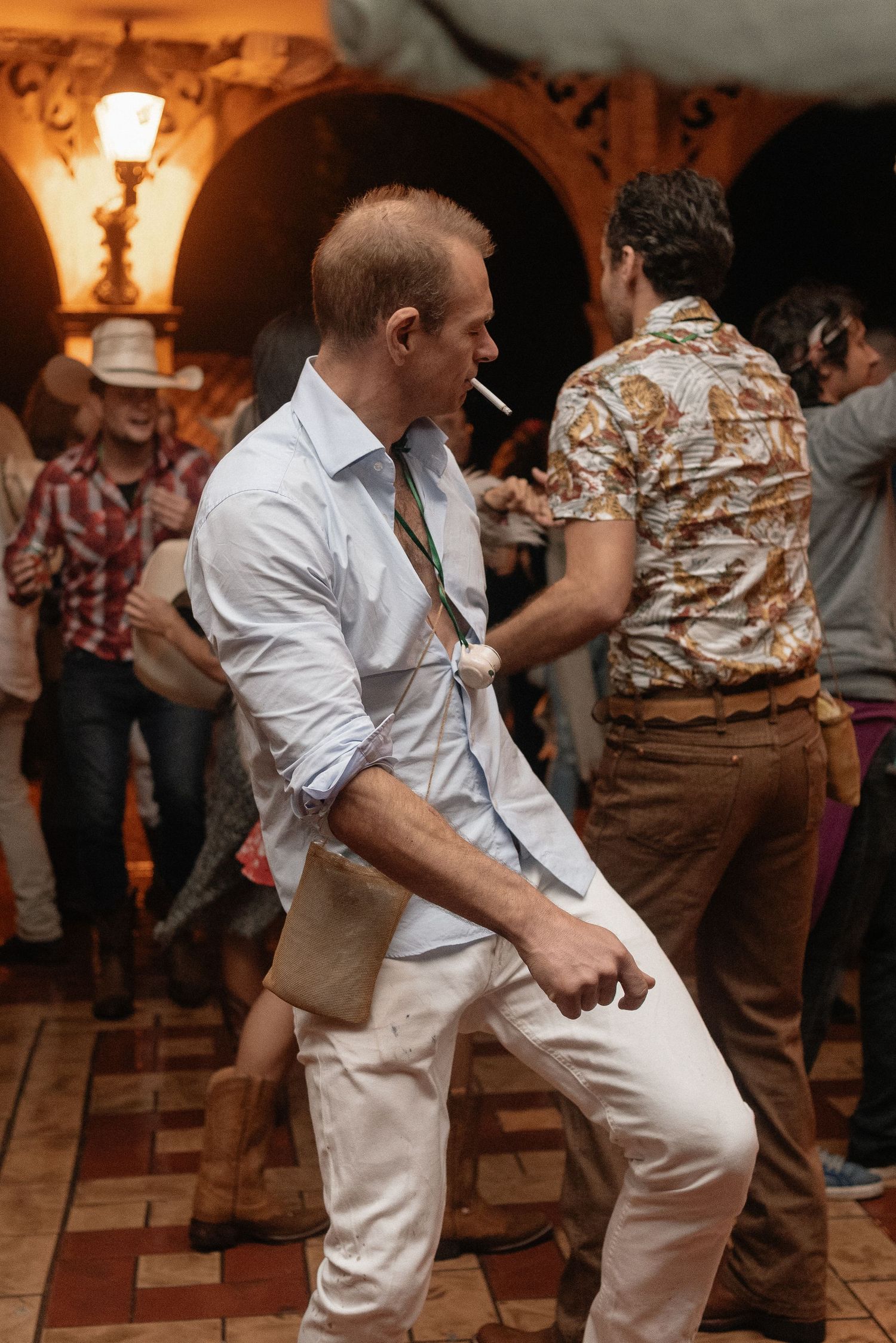 A dancer in a white outfit performs energetic retro dance moves on a vintage tiled floor beneath decorative archways.