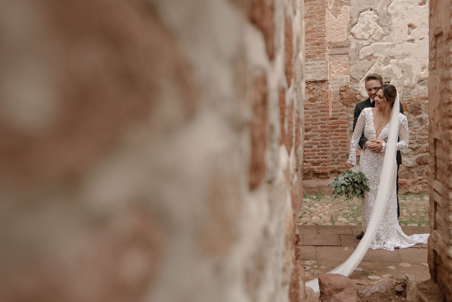 A romantic wedding couple embraces in a rustic stone archway with vintage brick walls and soft lighting.