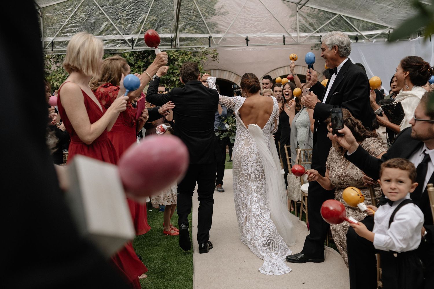 Wedding guests celebrate with bubbles during an outdoor ceremony under a tent as the couple walks down the aisle.