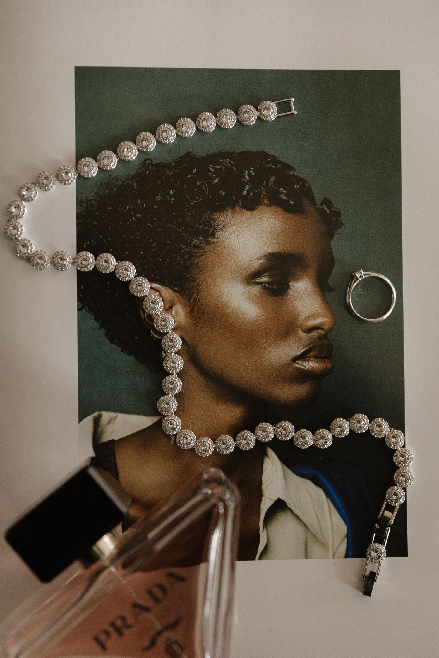 Diamond tennis necklace and bracelet styled on a fashion portrait with a Prada perfume bottle and silver ring.