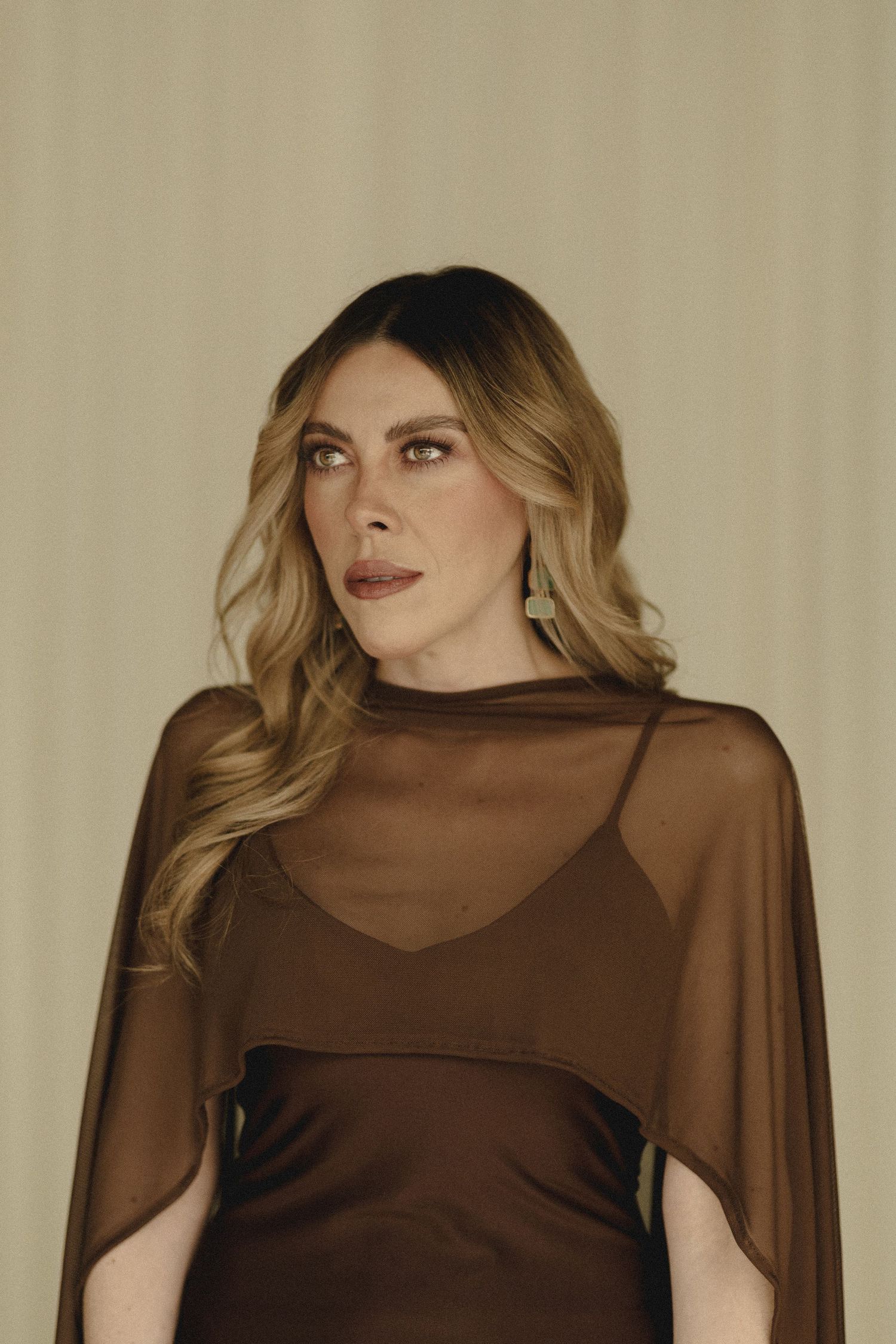 A model wears a sheer brown mesh top with dramatic poses against a beige backdrop in a fashion photoshoot series.