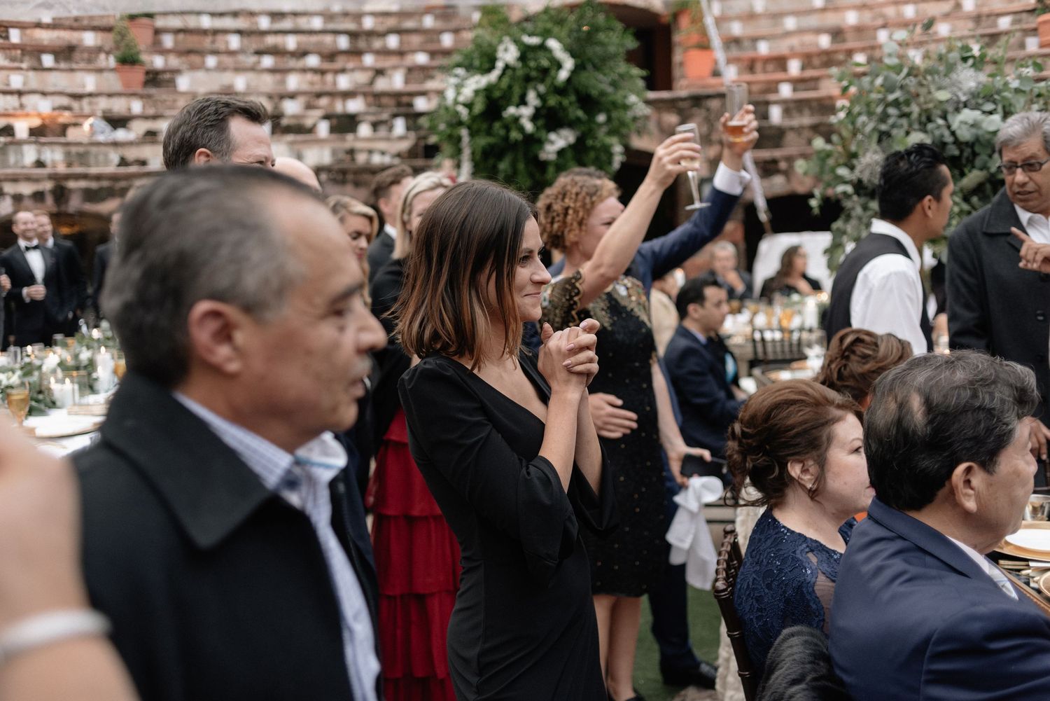 Guests enjoying drinks and socializing during an outdoor event against a brick wall backdrop.