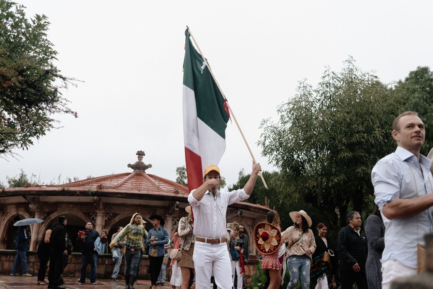 A demonstrator holds up an Irish flag at a public gathering while onlookers observe in front of a brick building.