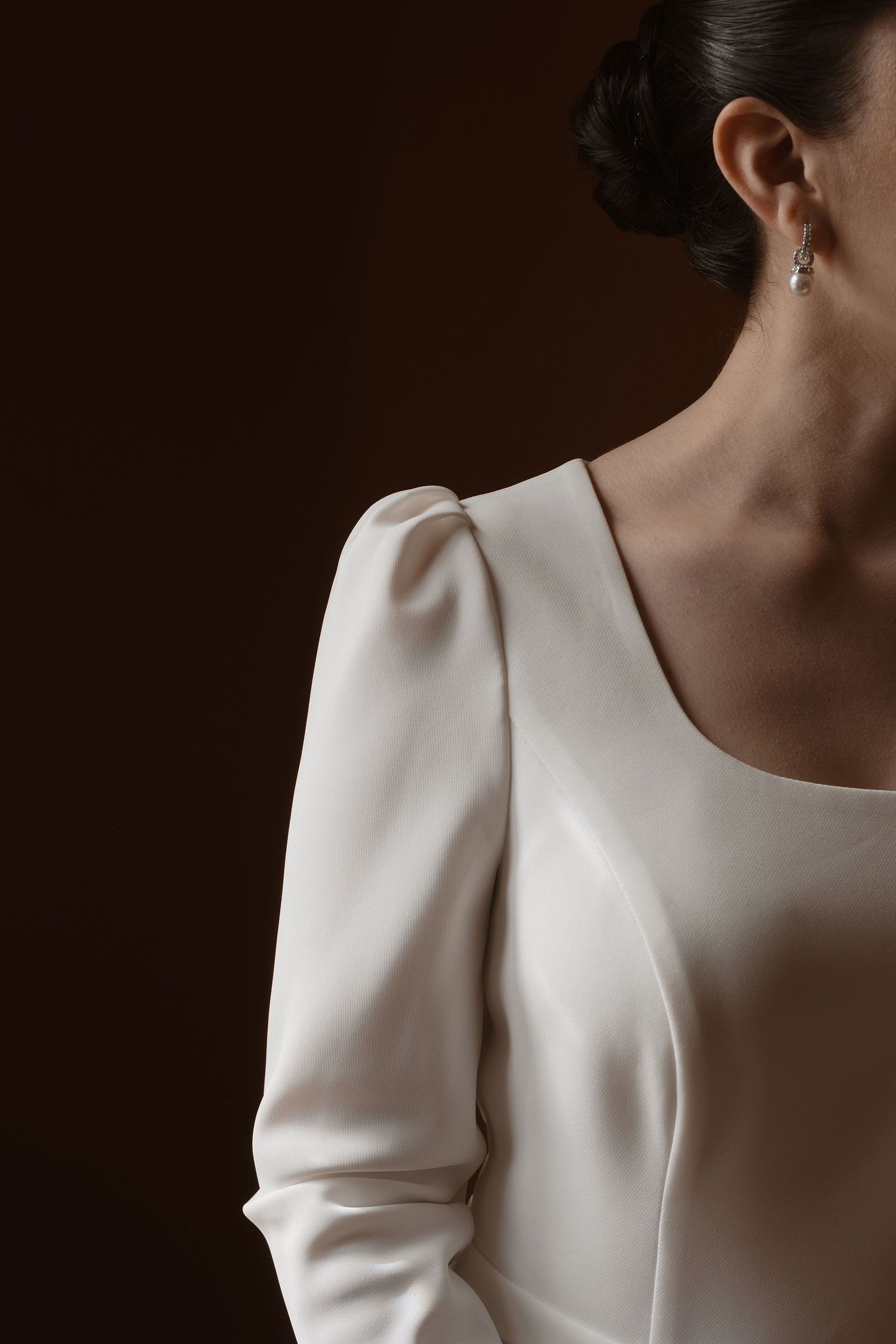 Close-up series of a minimalist white wedding dress with structured shoulder details against a dark background.