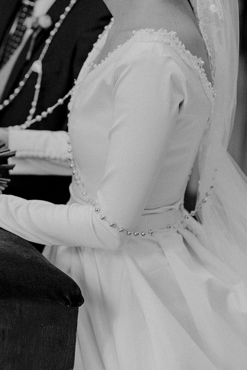Black and white close-up of vintage wedding dress showing detailed pearl buttons and long sleeves.