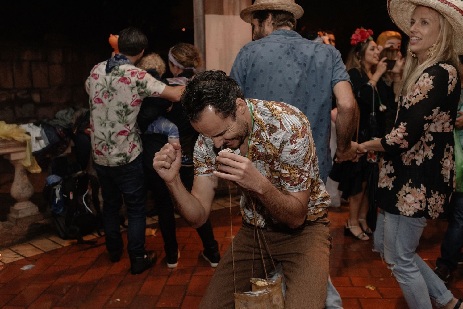 A group of people in floral shirts and cowboy hats dancing at a western-themed party on a wooden dance floor.