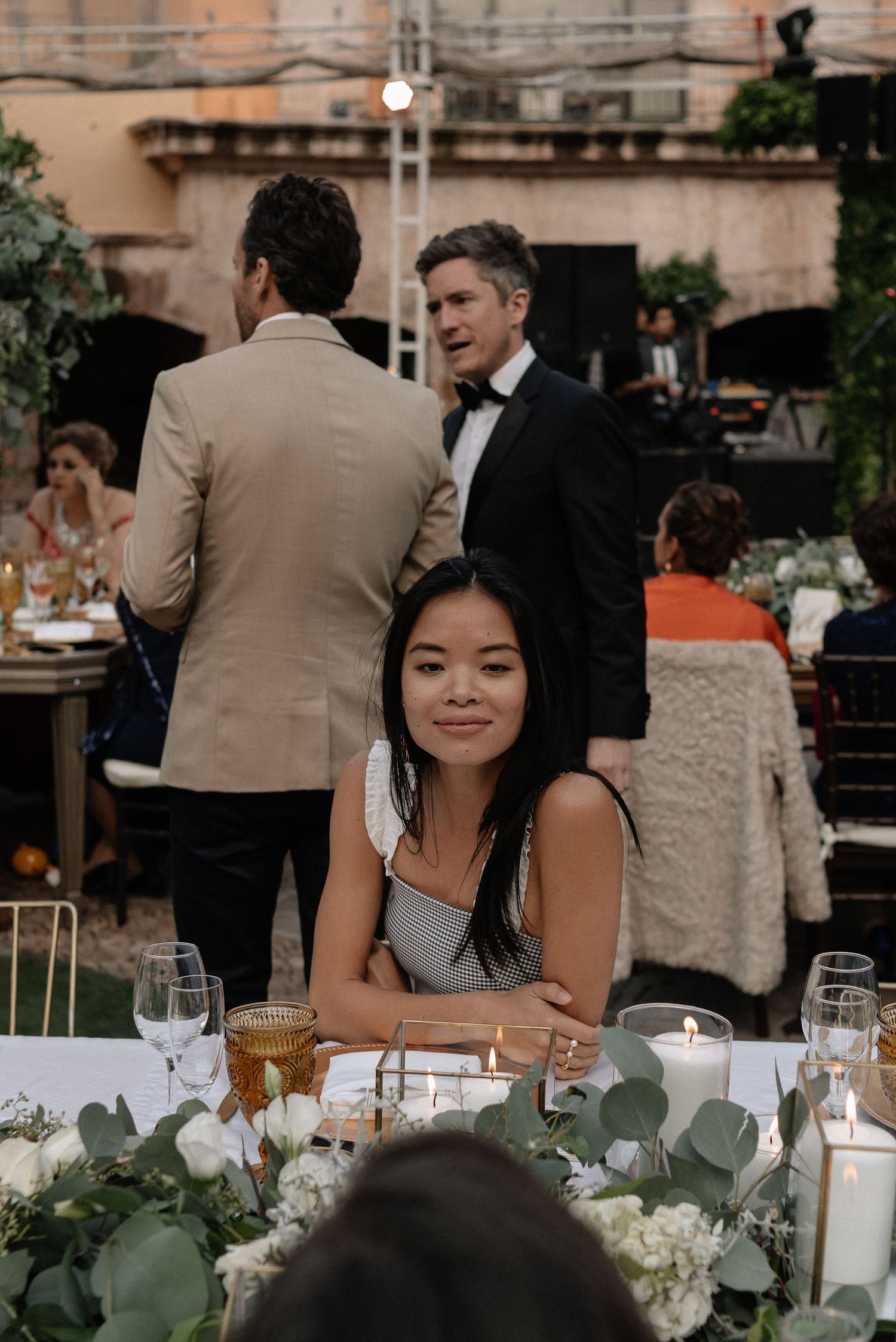 An outdoor wedding reception dinner table decorated with eucalyptus greenery, candles and elegant place settings.