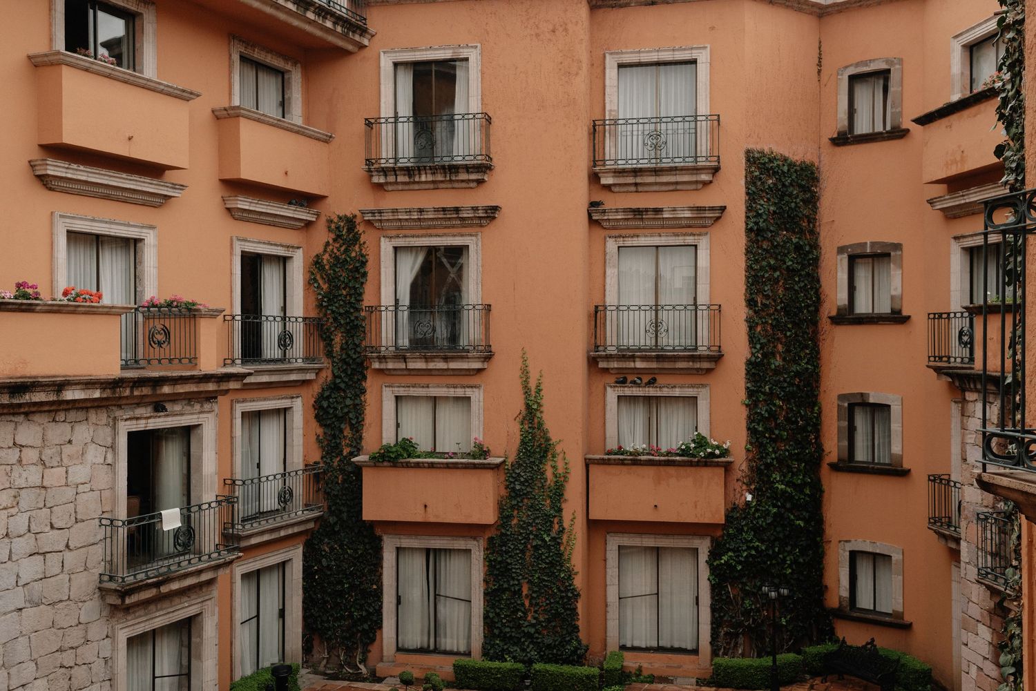 Mediterranean apartment building exterior with peach-colored walls, wrought iron balconies, and tall cypress trees.