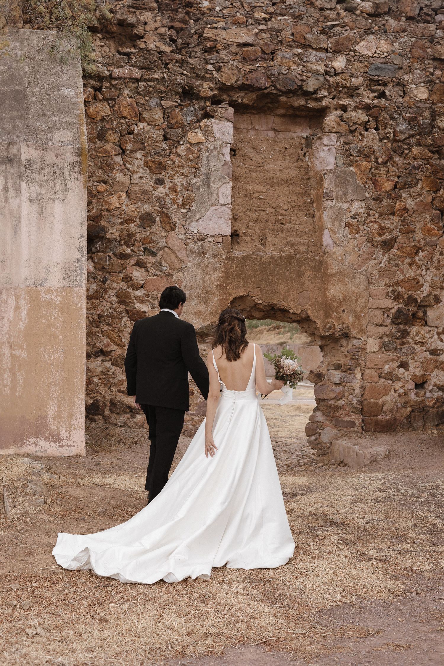 Couple walking along ancient stone ruins during their wedding photoshoot.