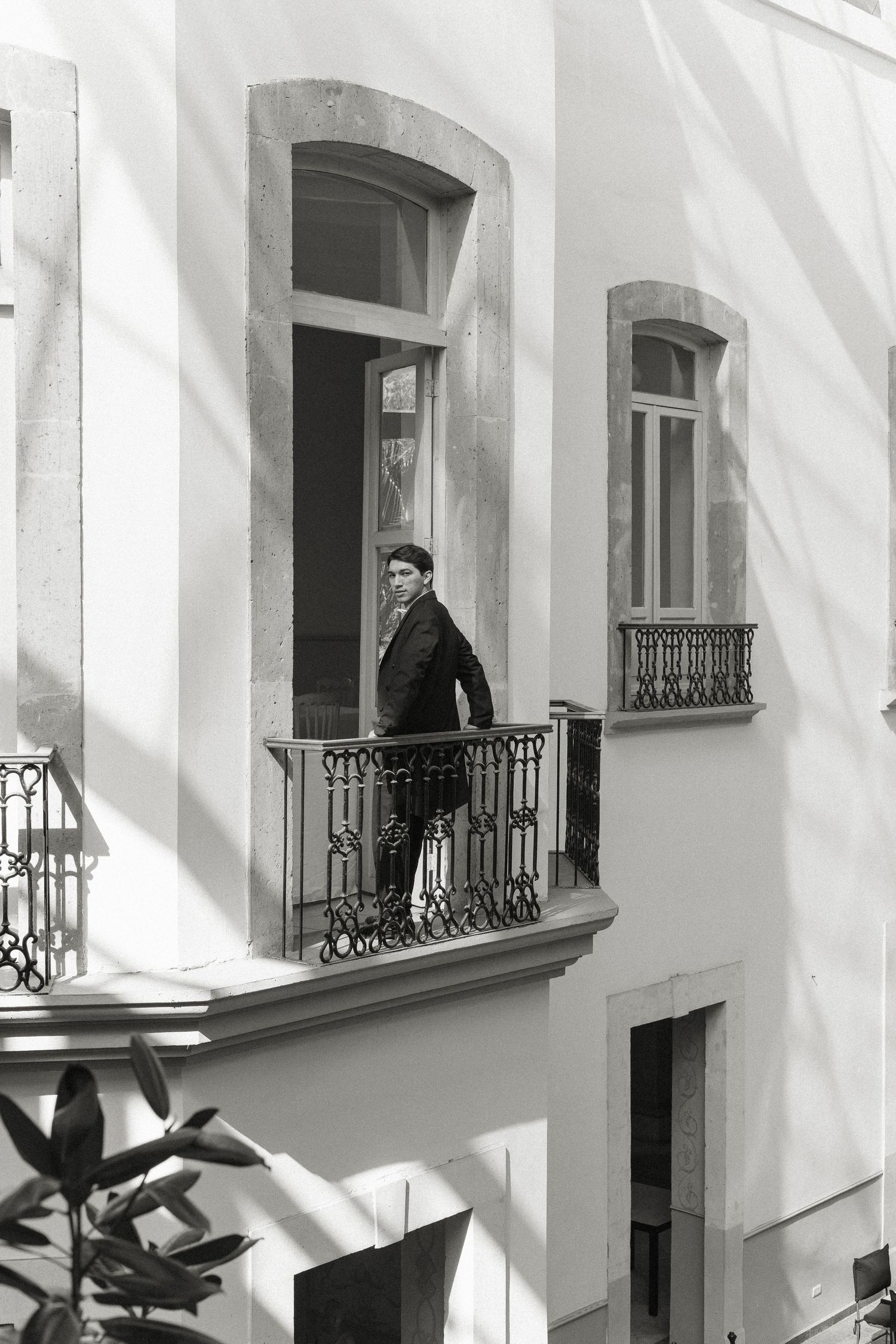 A black and white architectural photograph shows a repeating pattern of windows with ornate iron balconies on a white building.