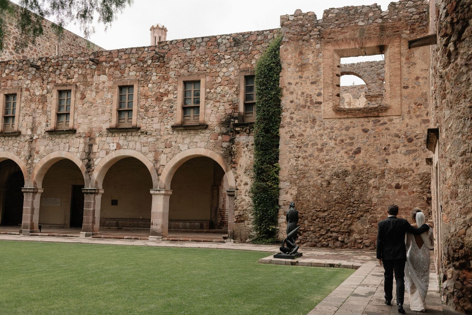 Historic stone arches and walls with ivy at Mission San Jose in San Antonio, with visitors exploring the courtyard.